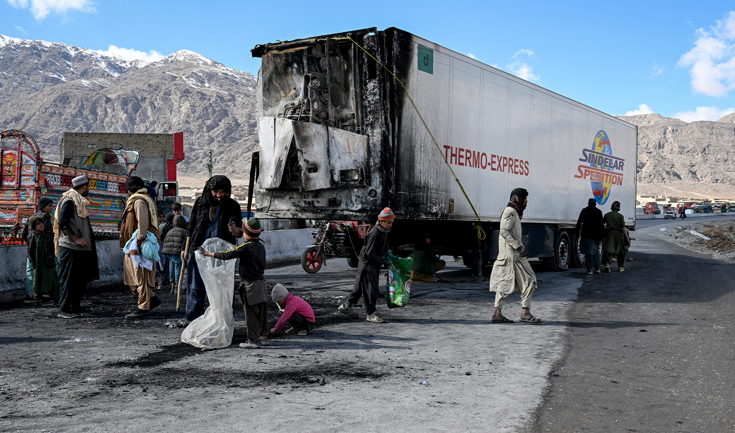 Bystanders walk past a burnt vehicle as others collect recyclables along a road on the outskirts of Quetta on February 1, 2026 a day after an attack by Baloch separatists. (AFP/File)