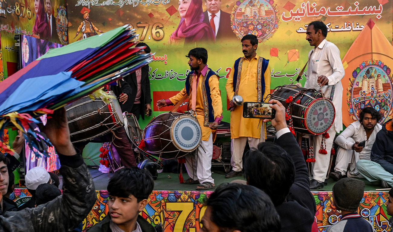 Artists play traditional drums next to a hoarding with portraits of Pakistan's former Prime Minister and leader of the Pakistan Muslim League Nawaz (PMLN) party Nawaz Sharif and his daughter and Chief Minister of the country's Punjab province Maryam Nawaz Sharif, as vendors sell kites to mark Basant Festival in Lahore on February 4, 2026. (AFP)