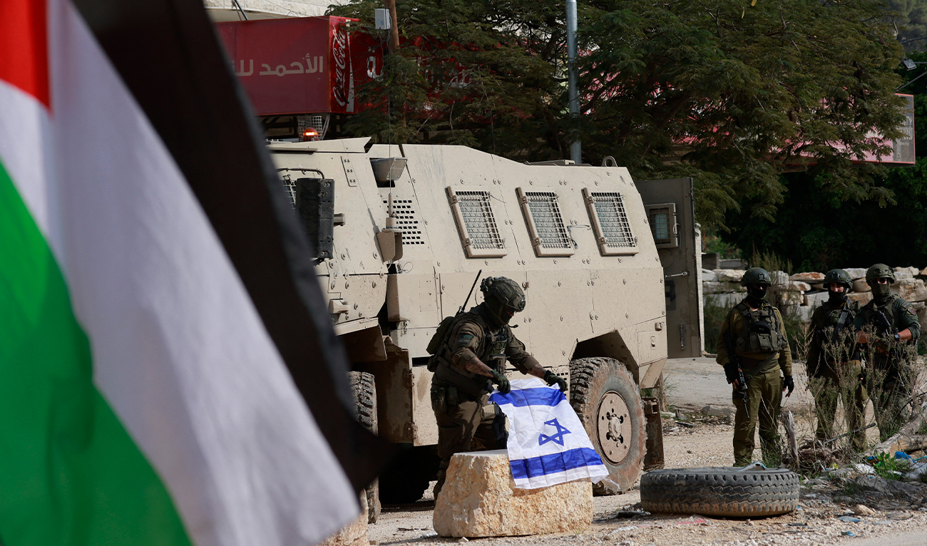 An Israeli soldier places the Israeli flag on a bollard at the entrance of the Nur Shams Palestinian refugee camp, in the Israeli-occupied northern West Bank on December 15, 2025. (AFP)