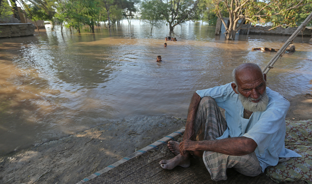 An elderly farmer sits while children swim in flood waters in Alipur, a town of Muzaffargarh district in Punjab province on September 12, 2025, after the Head Panjnad overflowed following heavy monsoon rains. (AFP/ File)