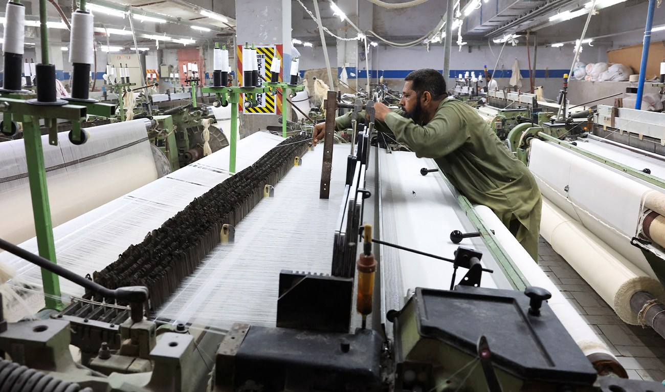 A worker examines cotton yarn threads while working on a loom machine, weaving fabric at a textiles manufacturer in Karachi, Pakistan April 3, 2025. (Reuters/File)