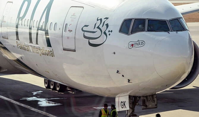 Ground staff stand next to the Pakistan International Airline (PIA) aircraft ahead of its takeoff for Paris at the Islamabad International Airport on January 10, 2025. (AFP/File)