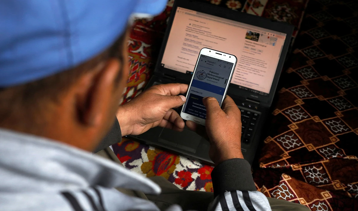 Tariq Jamil, 51, chairman of the Community Based Disaster Risk Management Centre, monitors a metrological website on his mobile phone and laptop, at home in Hassanabad village, Hunza valley, in the Karakoram mountain range in the Gilgit-Baltistan region of Pakistan, October 9, 2023.