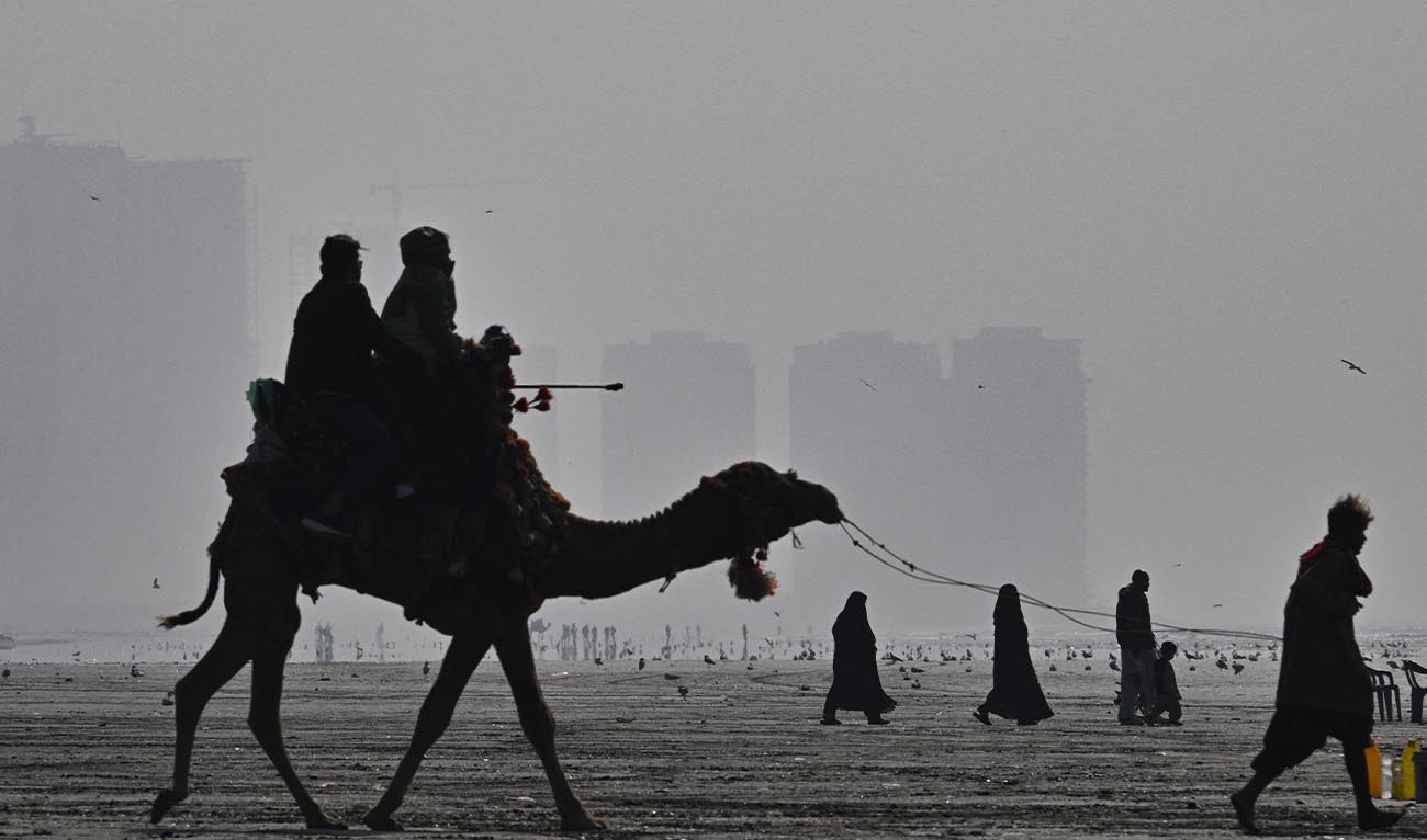 This photograph taken on January 10, 2026 shows people riding a camel amid dense smog at the Seaview Beach in Karachi. (AFP/ file)