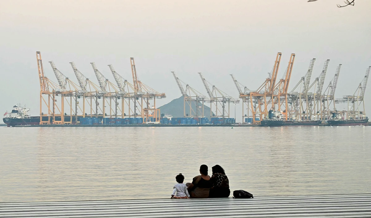 A family sits against the backdrop of a dockyard off coast city of Fujairah, in the Strait of Hormuz in the northern Emirate on February 25, 2026. (AFP)