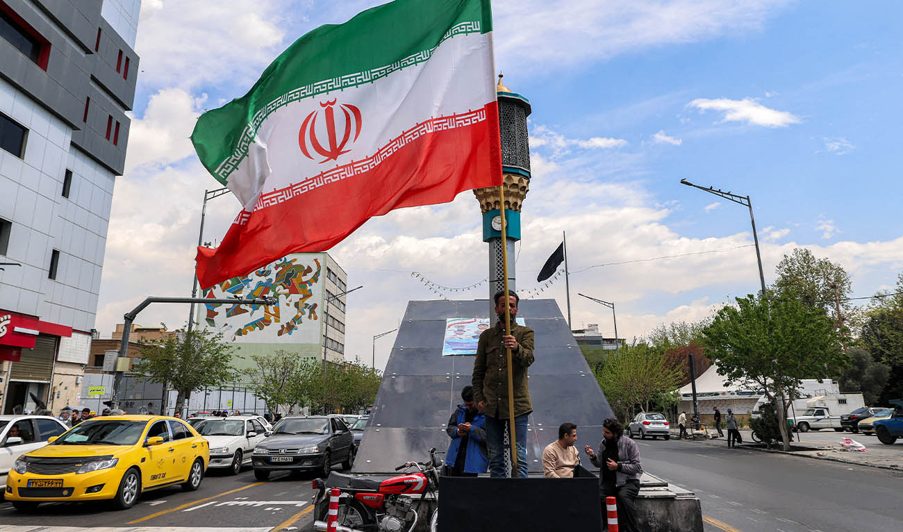 A man stands with an Iranian national flag along an intersection at Valiasr Square in Tehran on April 6, 2026. (AFP)