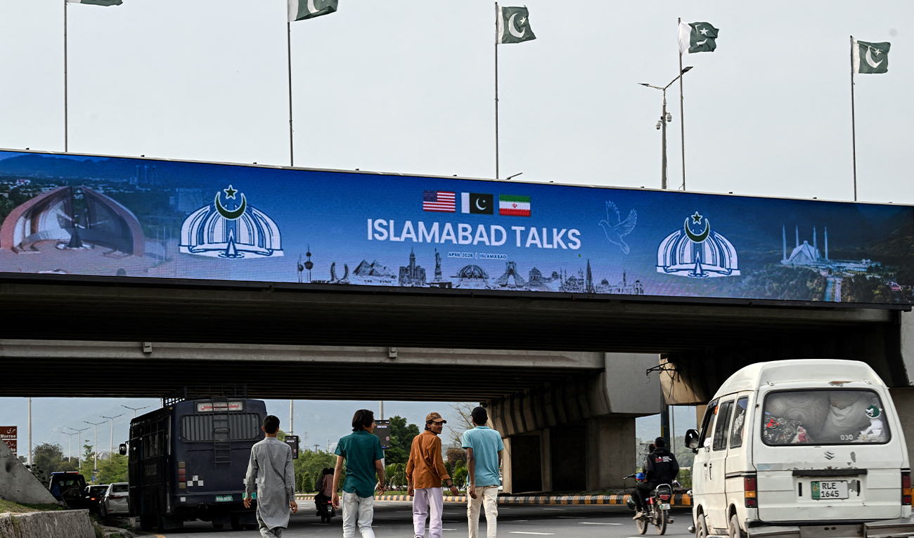 People walk under a digital screen displaying news of US–Iran peace talks along a road in Islamabad, Pakistan, on April 10, 2026. (AFP)