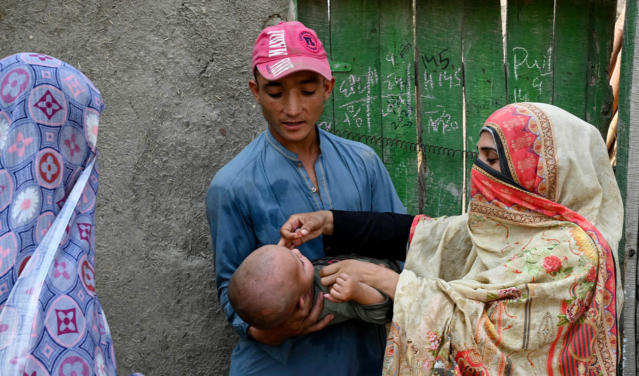 This photograph taken on October 5, 2024 shows a health worker (R) administering polio drops to a child during a door-to-door poliovirus vaccination campaign on the outskirts of Peshawar.