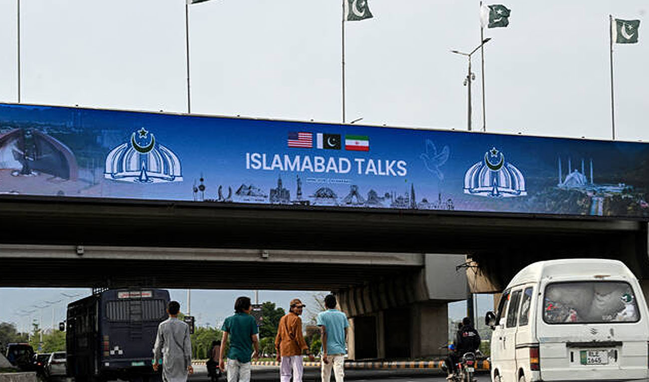 People walk under a digital screen displaying news of US–Iran peace talks along a road in Islamabad, Pakistan, on April 10, 2026. (AFP/File)