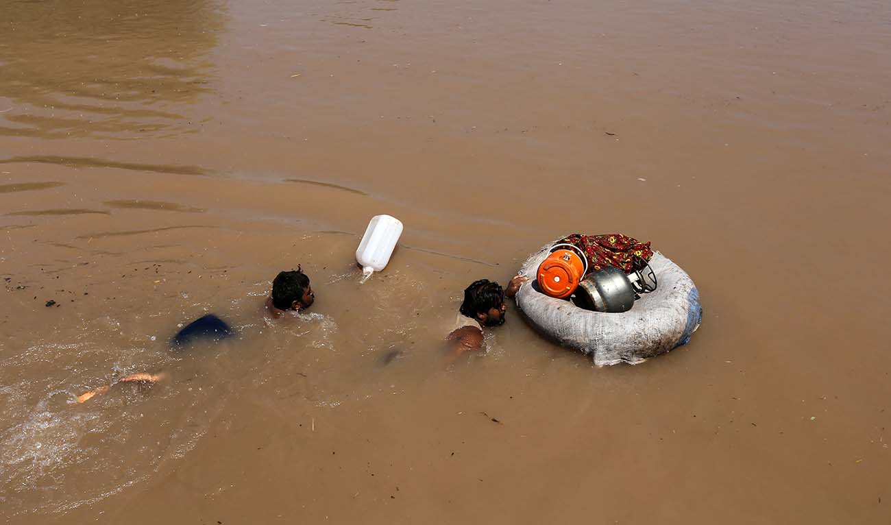Villagers with their belongings swim through the floodwaters at Alipur in the Muzaffargarh district of Punjab province on September 13, 2025, after the Head Panjnad, the confluence of five rivers Jhelum, Chenab, Ravi, Beas and Sutlej overflowed owing to heavy monsoon rains. (AFP/ file)