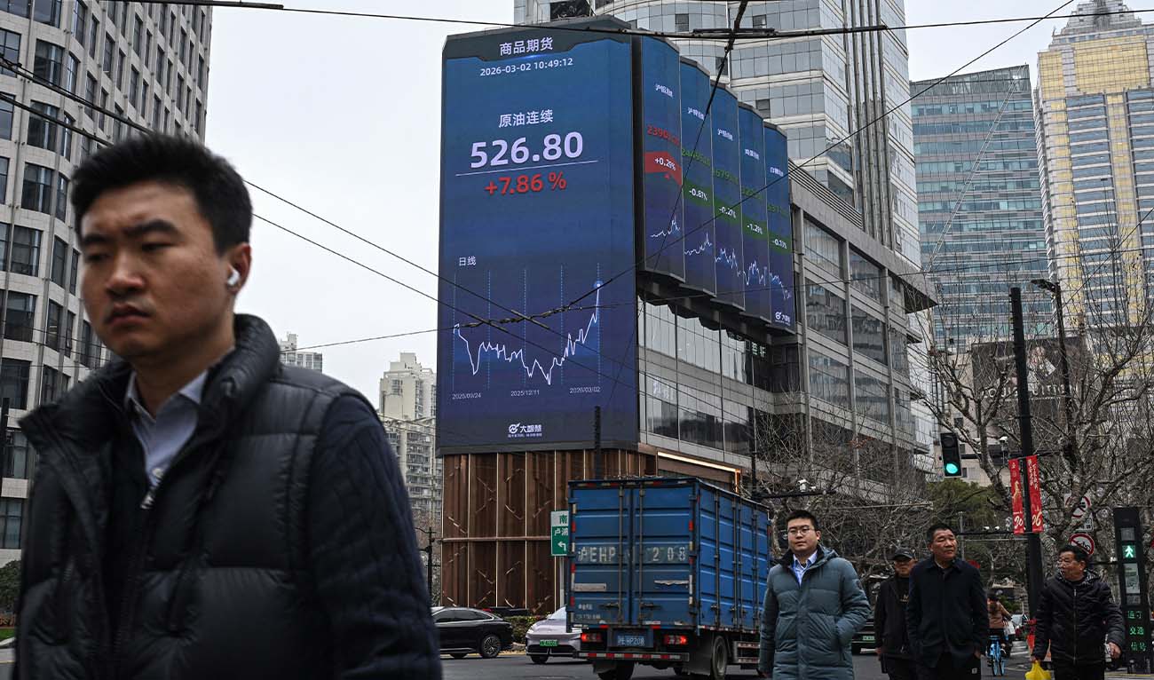 Pedestrians walk next to a screen showing the commodity futures for crude oil in the Jing'an district of Shanghai on March 2, 2026. (AFP/ file)