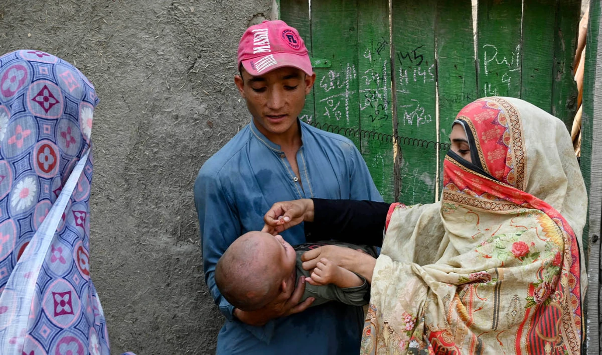 This photograph taken on October 5, 2024 shows a health worker (R) administering polio drops to a child during a door-to-door poliovirus vaccination campaign on the outskirts of Peshawar.