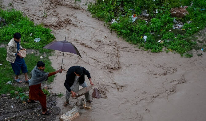 Residents use stones to cross a path flooded by an overflowing rainwater channel following heavy rains in Peshawar on April 7, 2026. (AFP/File)