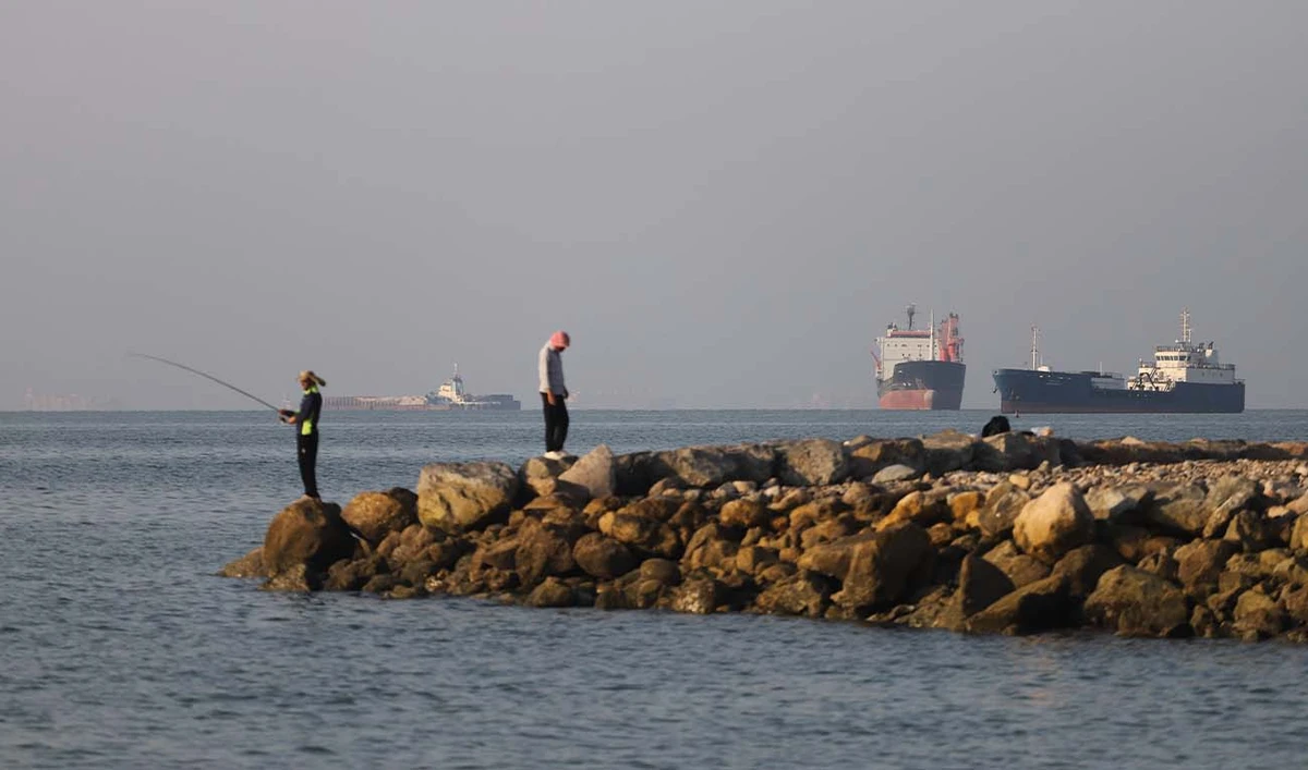 In this picture obtained from Iran's ISNA news agency on June 8, 2026, residents fish from the shore as cargo and commercial vessels lie at anchor in the Strait of Hormuz off Bandar Abbas on June 8, 2026. (AFP/ file)