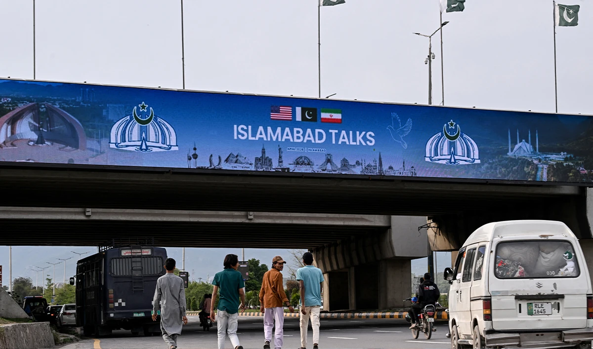 Boys walk under a digital screen displaying news of US-Iran peace talks along a road in Islamabad, Pakistan, on April 10, 2026. (AFP/File)