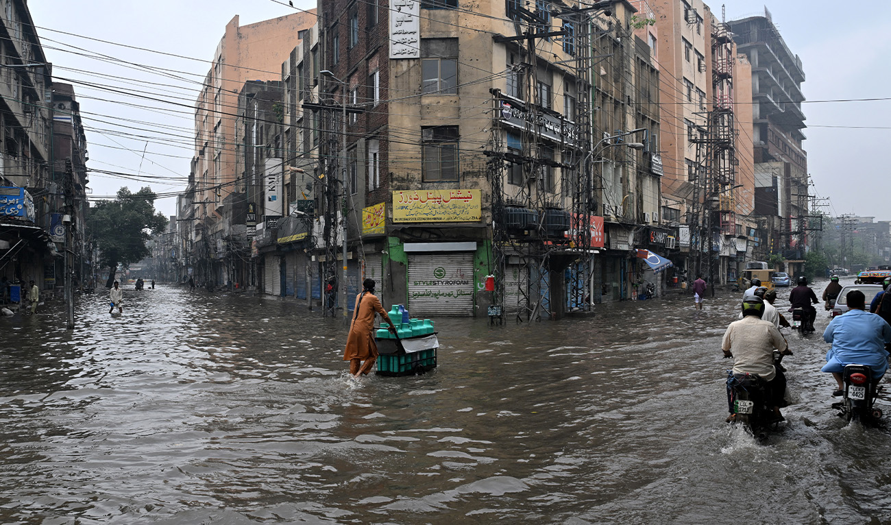 Commuters wade through a flooded street after heavy rainfall in Lahore on July 25, 2026. (AFP)