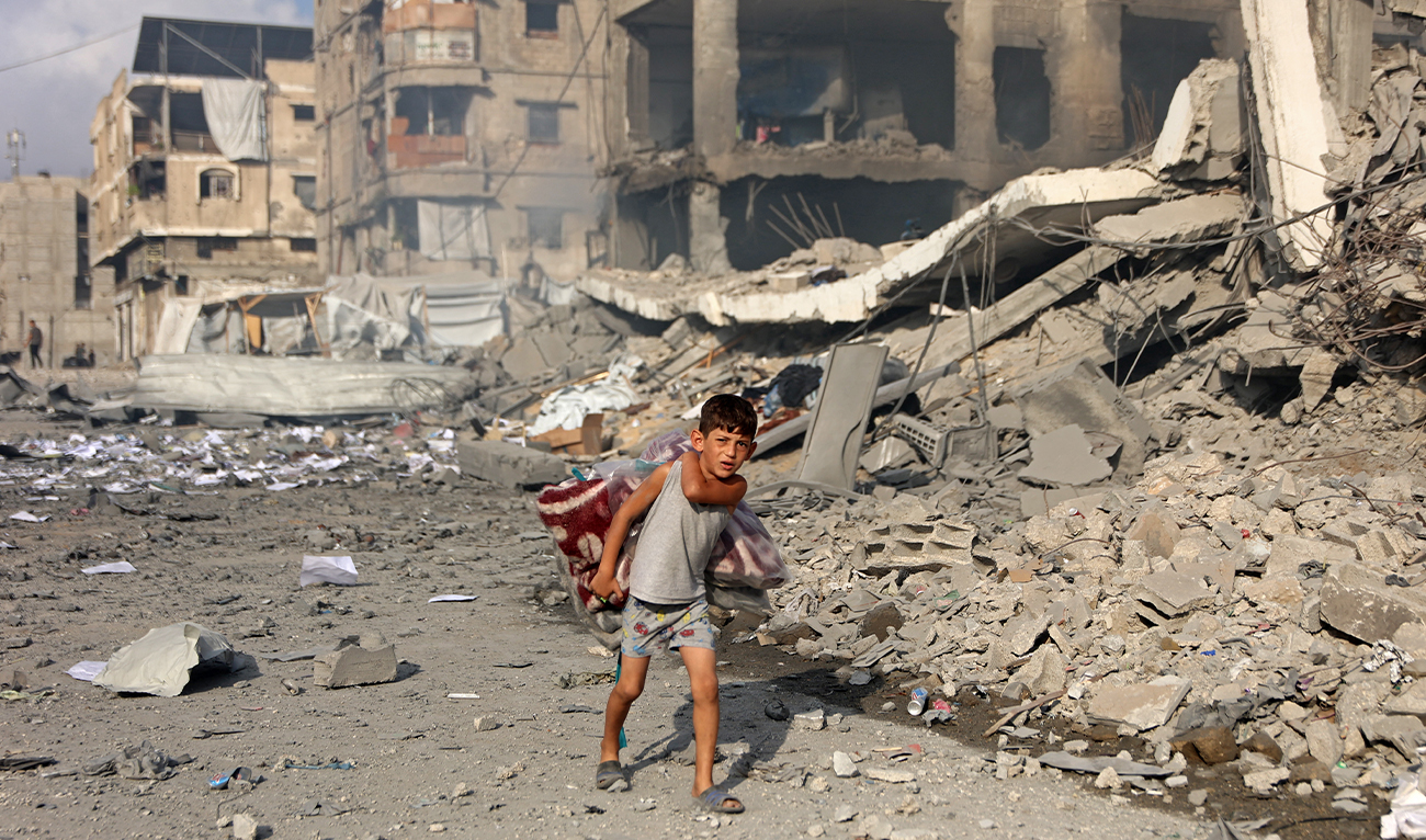Graphic content / A Palestinian boy carrying a quilt walks past the destroyed buildings at the Al-Jalaa street following an Israeli strike in Gaza City on July 24, 2026. (AFP)