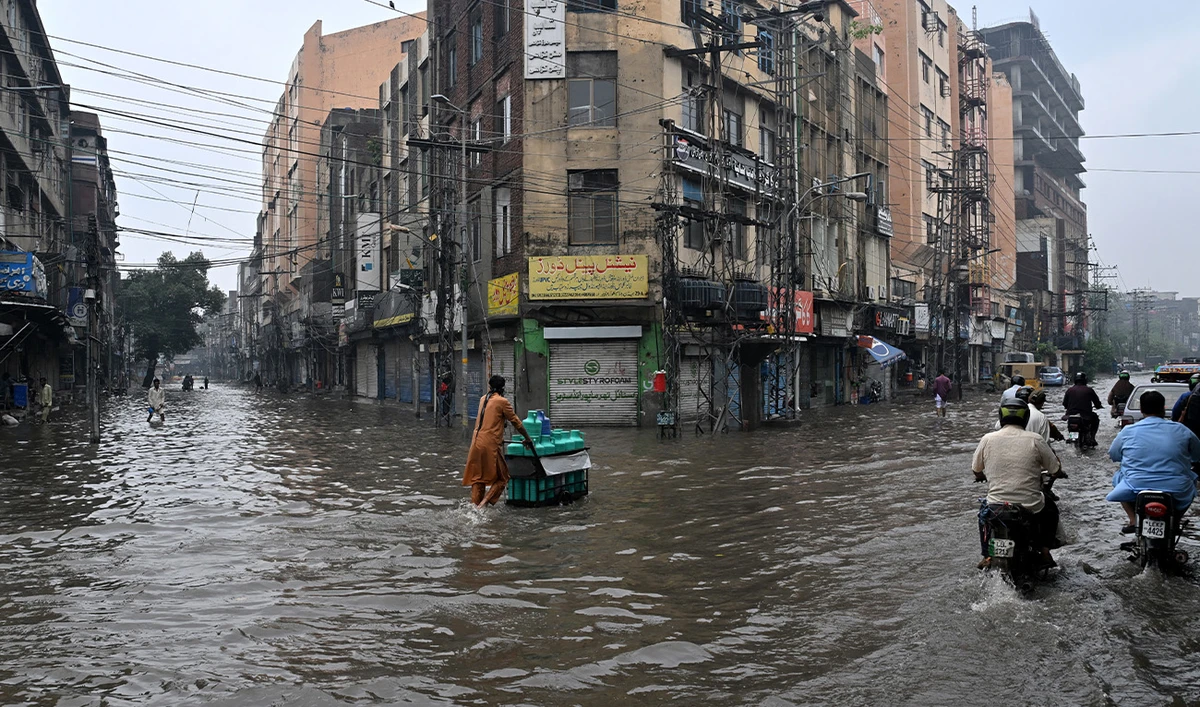 Commuters wade through a flooded street after heavy rainfall in Lahore on July 25, 2026. (AFP)