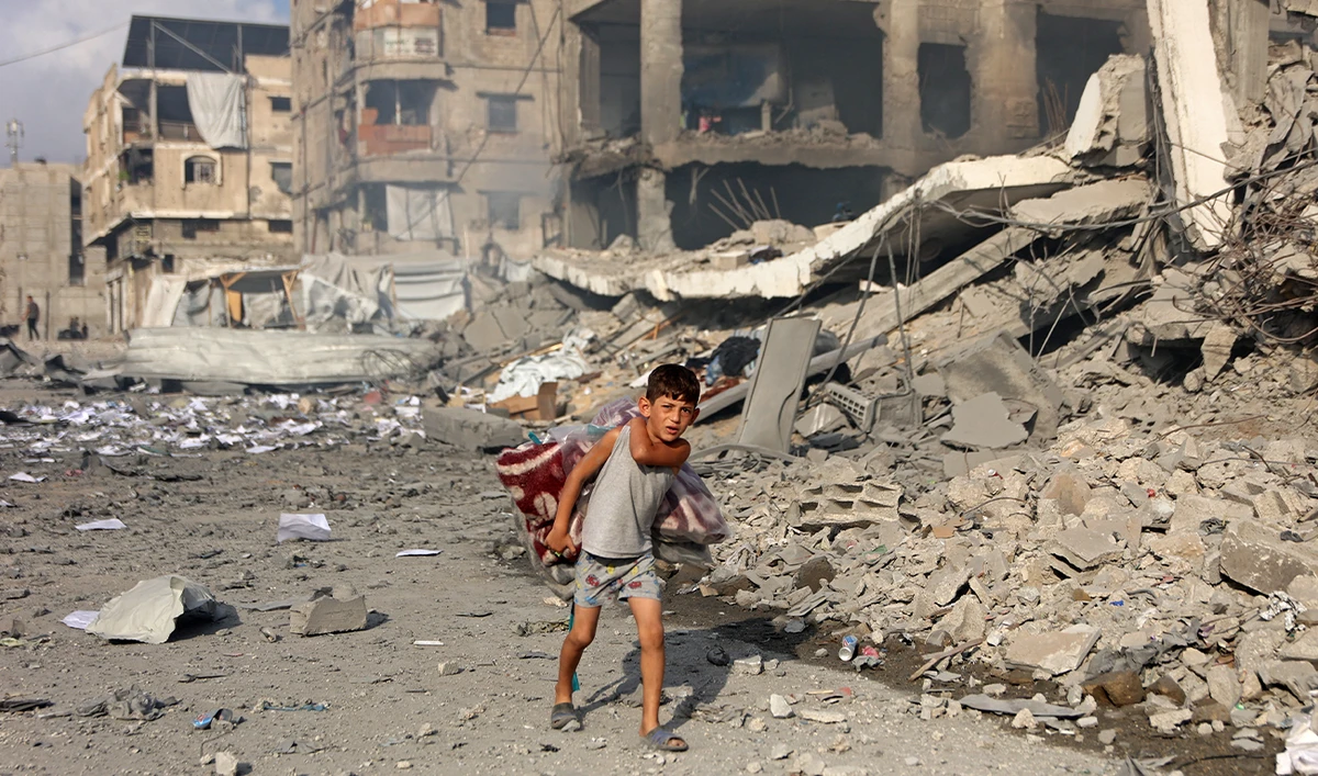 Graphic content / A Palestinian boy carrying a quilt walks past the destroyed buildings at the Al-Jalaa street following an Israeli strike in Gaza City on July 24, 2026. (AFP)