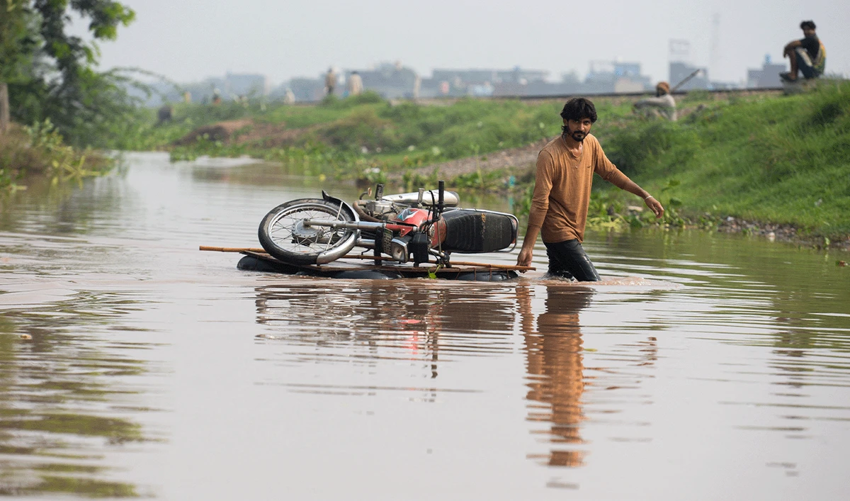 A man pulls his motorcycle across a wooden plank through floodwaters following monsoon rains in Ferozwala, Pakistan, July 30, 2026. (Reuters)