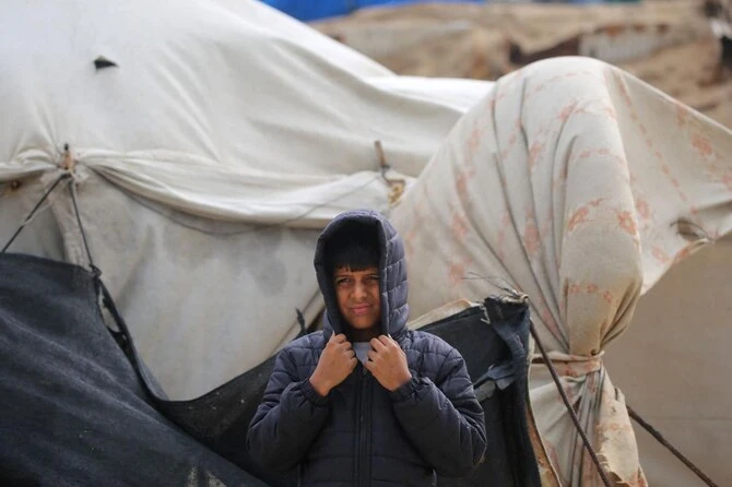 2024年12月20日、イスラエルとハマスの戦争が続く中、ガザ地区中部のヌセイラット難民近くの海岸にある国内避難民キャンプで、風に吹かれながら頭を覆うパレスチナの少年。(AFP=時事)