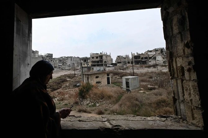 A displaced Syrian stands inside her dilapidated apartment, overlooking the destruction in Homs' Khaldiyeh neighborhood. (AFP)