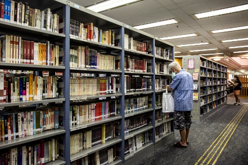 Un homme cherche un livre dans une bibliothèque publique de Hong Kong. Les ouvrages des activistes de la démocratie disparaissent des rayons. (Isaac LAWRENCE/AFP)
