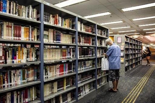 Un homme cherche un livre dans une bibliothèque publique de Hong Kong. Les ouvrages des activistes de la démocratie disparaissent des rayons. (Isaac LAWRENCE/AFP)