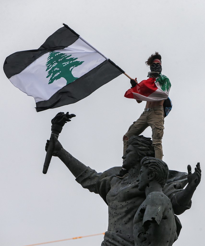 Un manifestant tenant un drapeau libanais à rayures noires se dressant au sommet de la statue des martyrs lors d'une manifestation anti-gouvernementale le 1er septembre 2020. (AFP)