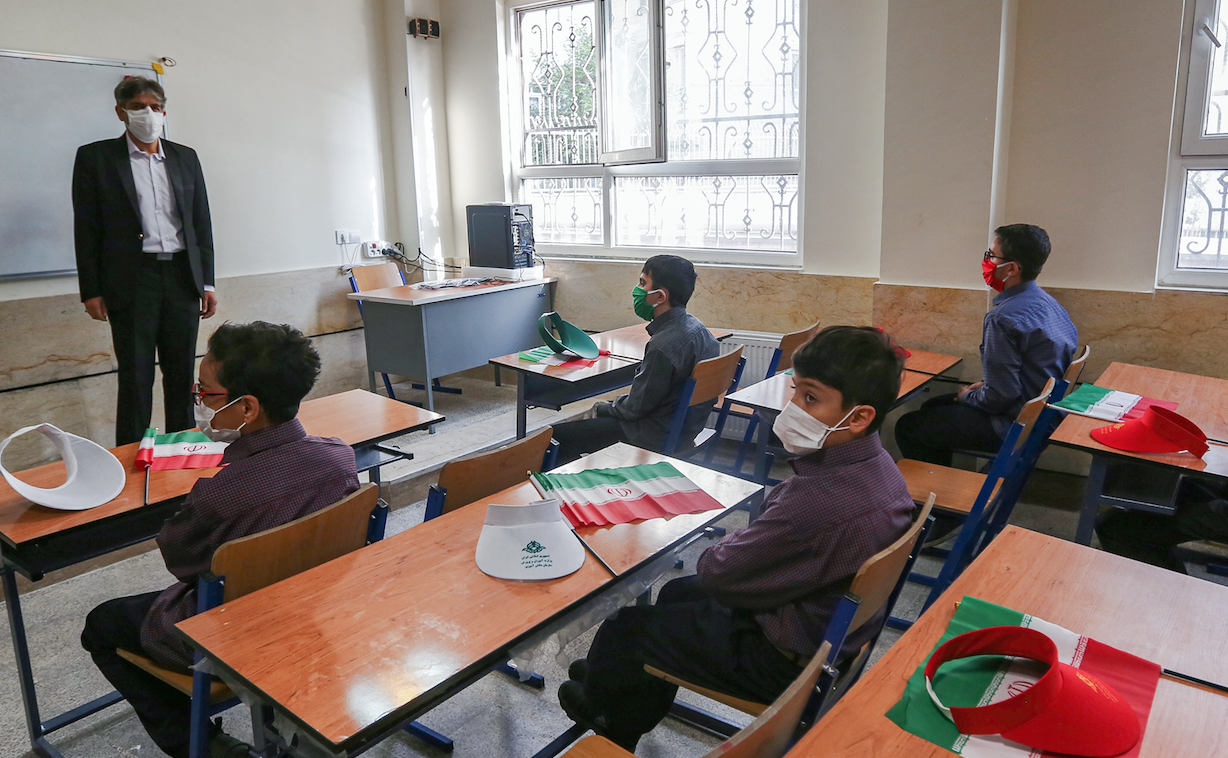 Le premier jour de la réouverture des écoles, à l'école de Nojavan dans la capitale Téhéran. Les écoliers sont vêtus de masques et éloignés les uns des autres, avec des drapeaux nationaux iraniens sur le bureau de chacun. (Atta Kenare / AF)