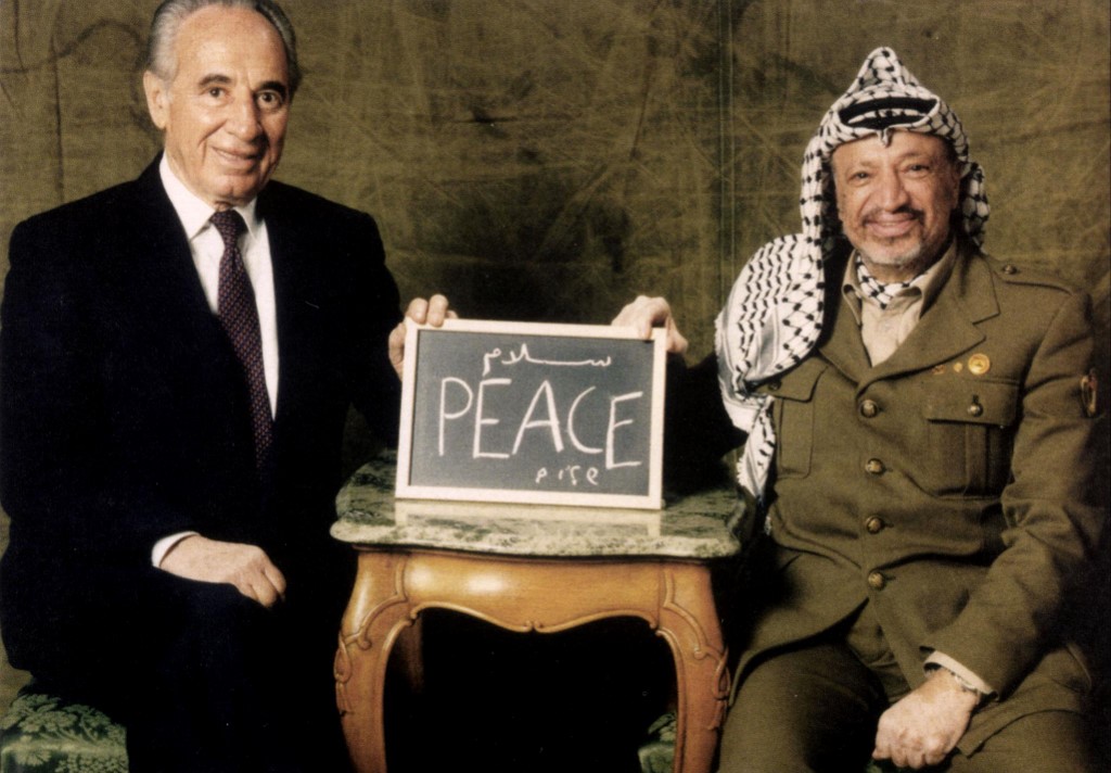 Yasser Arafat, alors Président de l’Autorité palestinienne et Shimon Peres, ministre des Affaires étrangères israélien, posaient ensemble – entre eux, il est écrit « Paix » (Photo, PPO/AFP).