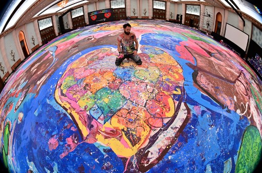 L’artiste contemporain Sacha Jafri assis sur sa peinture monumentale « The Journey of Humanity » à Dubai. (Giuseppe Cacace/AFP)