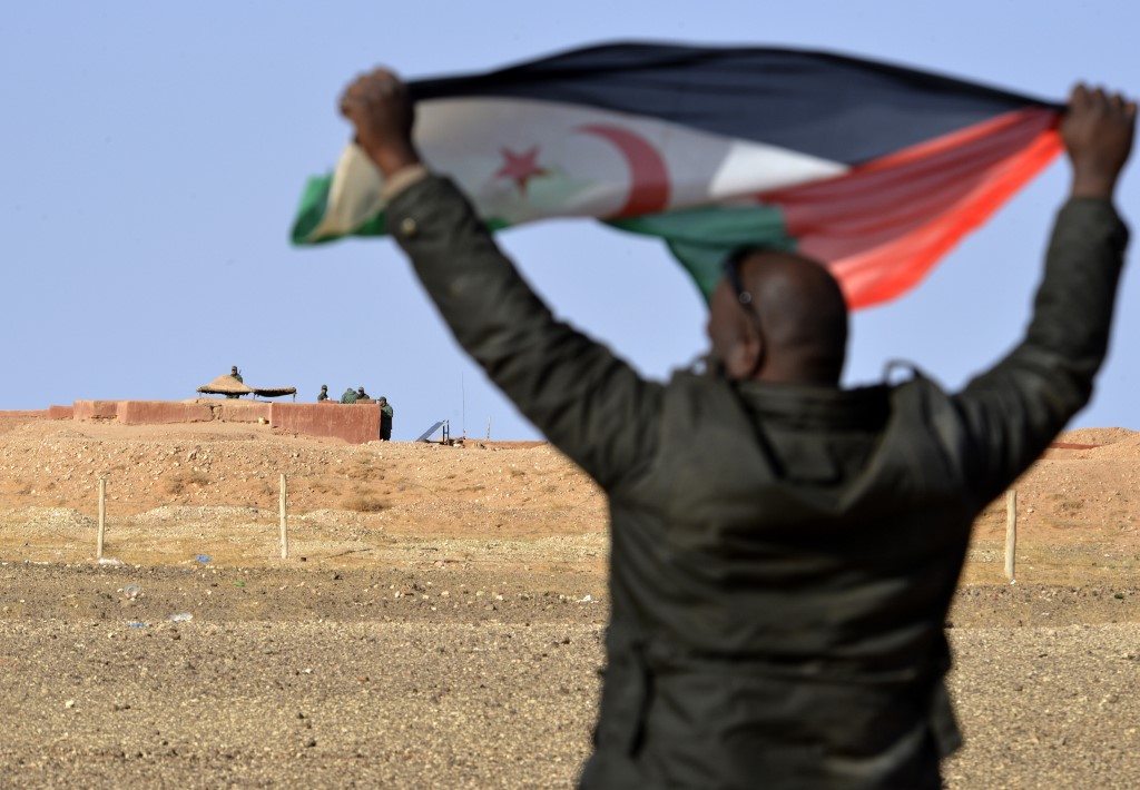 Sur cette photo prise le 3 février 2017, un homme sahraoui brandit un drapeau du Front Polisario dans la zone d'Al-Mahbes près de soldats marocains gardant le mur séparant le Sahara occidental contrôlé par le Polisario du Maroc. (AFP)
