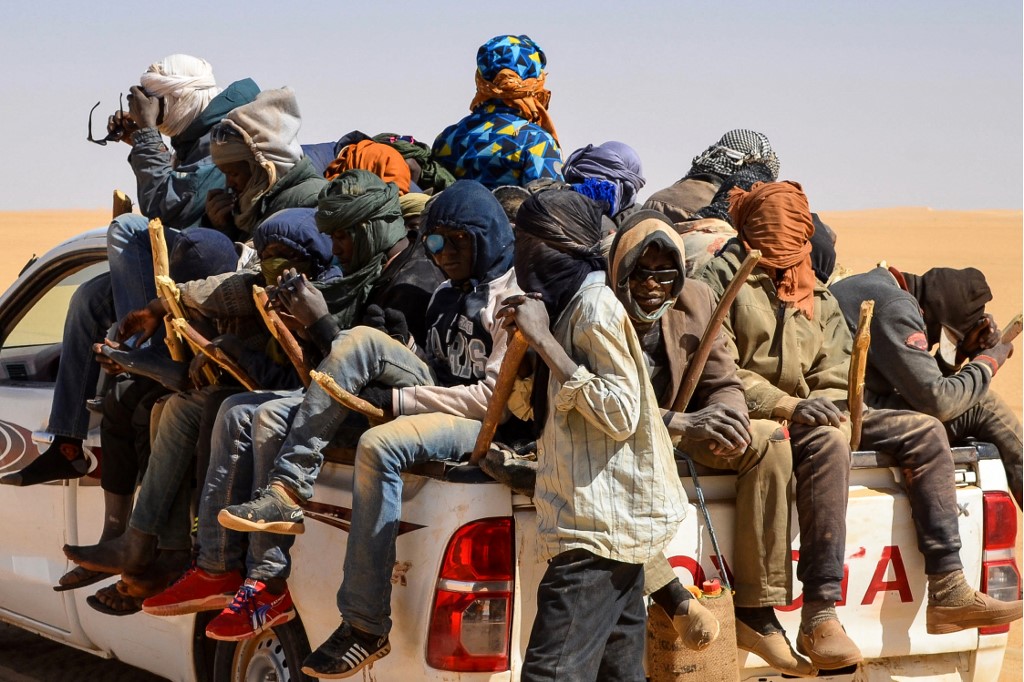Un groupe d'hommes migrants, principalement du Niger et du Nigéria, est assis à l'arrière d'un pick-up, le 22 janvier 2019, lors d'un voyage à travers le désert de l'Air, au nord du Niger, en direction du poste frontière libyen de Gatrone. (AFP)