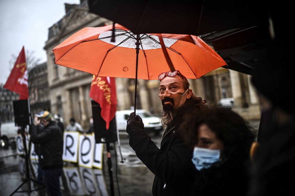 Un homme tient portant une maquette de masque protecteur tient un parapluie lors d'une manifestation convoquée par la Fédération CGT Spectacles devant le Conseil d'Etat à Paris le 21 décembre 2020, pour protester contre la fermeture d'entreprises culturelles pour freiner la propagation de la Covid-19. (AFP)