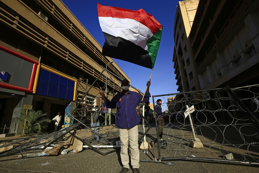 Un Soudanais agite le drapeau national de son pays alors qu'il se tient devant une rue barricadée lors des manifestations dans la capitale Khartoum pour marquer le deuxième anniversaire du début d'une révolte qui a renversé le gouvernement précédent, le 19 décembre 2020. (AFP)