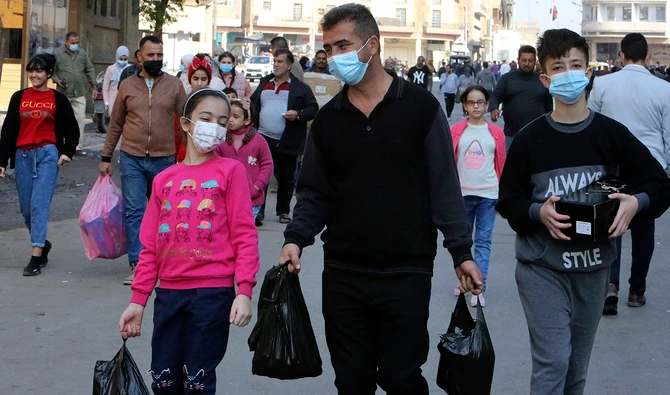 Des Irakiens portant des masques faciaux au milieu de la pandémie de Covid-19, marchent avec leurs achats dans la capitale Bagdad, le 4 décembre 2020 (AFP)