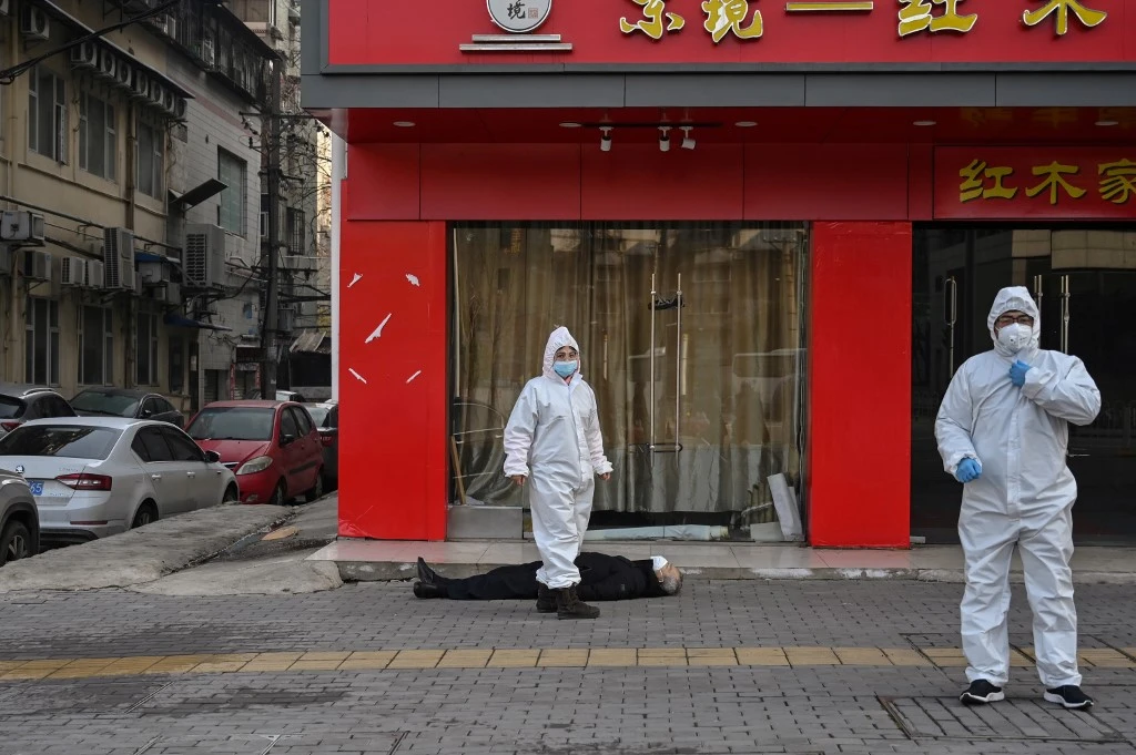 Cette photo prise le 30 janvier 2020 montre des responsables en tenue de protection vérifiant un homme âgé portant un masque facial qui s'est effondré et est décédé dans une rue près d'un hôpital de Wuhan. (HECTOR RETAMAL / AFP)