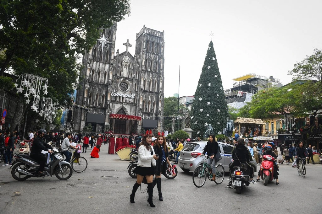 Des femmes portant des bandeaux sur le thème des rennes passent devant un arbre de Noël exposé devant la cathédrale Saint-Joseph de Hanoï, le 24 décembre 2020. (AFP)