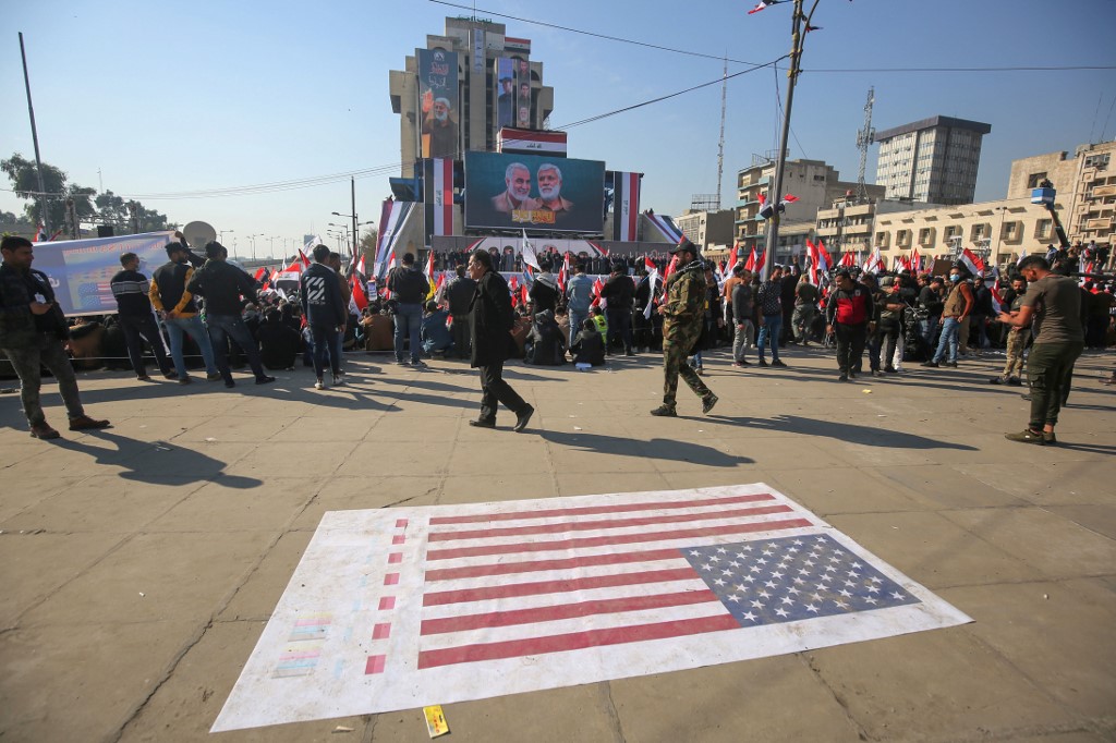 Des manifestants irakiens lèvent des drapeaux et des pancartes alors qu'ils se rassemblent sur la place Tahrir dans la capitale Bagdad le 3 janvier 2021. (AFP)