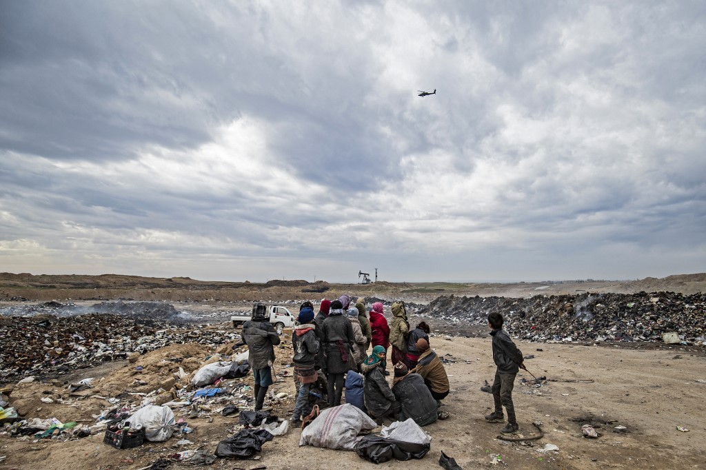 Un hélicoptère de l'armée américaine plane alors que des Syriens passent au crible une décharge près d'un champ pétrolifère dans la campagne de Malikiya, dans le nord-est de la Syrie, le 17 janvier 2021. (AFP)