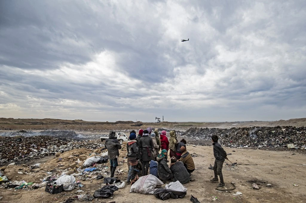 Un hélicoptère de l'armée américaine plane alors que des Syriens passent au crible une décharge près d'un champ pétrolifère dans la campagne de Malikiya, dans le nord-est de la Syrie, le 17 janvier 2021. (AFP)