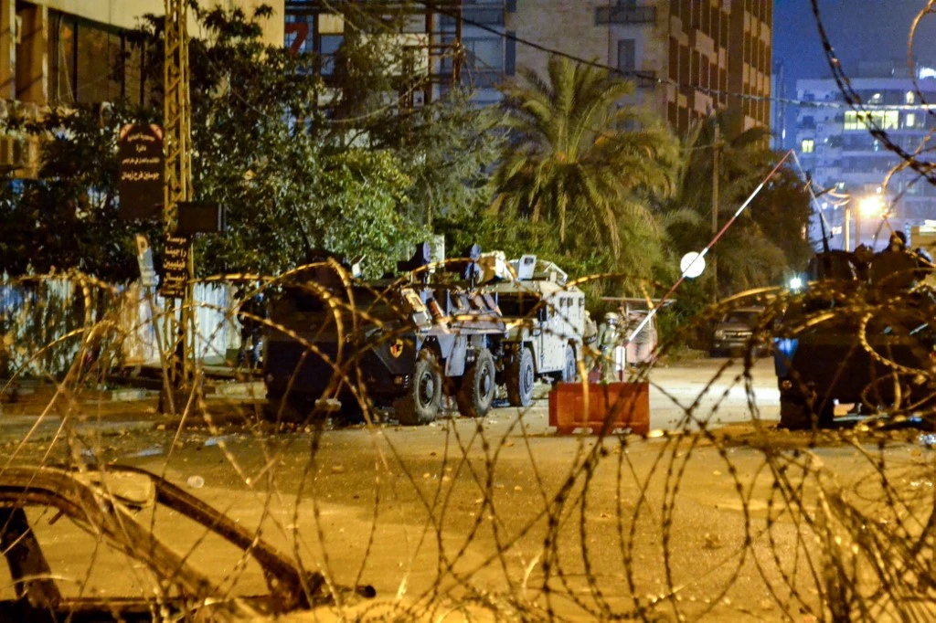 Des manifestants anti-gouvernementaux se mettent à couvert derrière des bennes à ordures lors d'affrontements avec les forces de sécurité dans le centre de la ville portuaire appauvrie de Tripoli. (AFP)