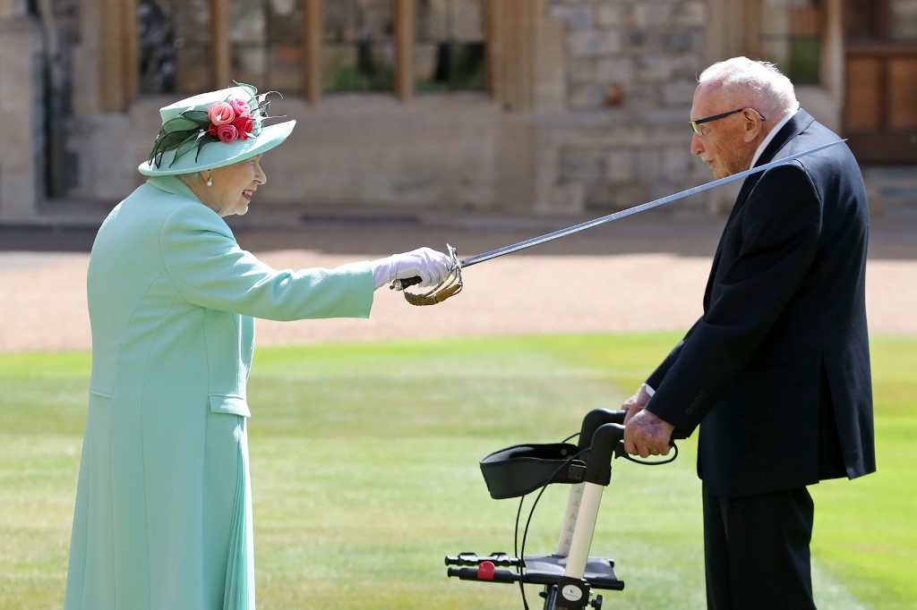 Dans ce fichier photo pris le 17 juillet 2020, la reine britannique Elizabeth II utilise l'épée qui appartenait à son père, George VI, alors qu'elle confère l'honneur de chevalerie au capitaine Tom Moore, vétéran de la Seconde Guerre mondiale, âgé de 100 ans, au château de Windsor à Windsor, dans l'ouest de Londres le 17 juillet 2020. (AFP)
