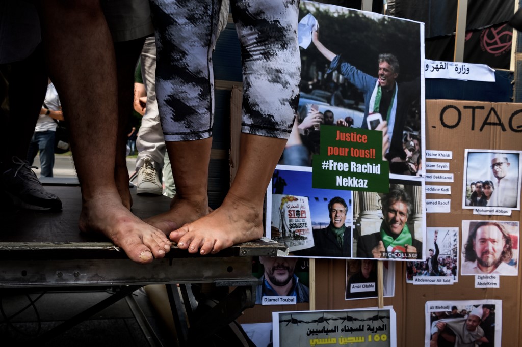 Des militants proches du mouvement de contestation algérien "Hirak" se tiennent pieds nus à côté de photos de prisonniers lors d'une manifestation devant les bureaux des Nations Unies à Genève contre les "arrestations arbitraires" en Algérie, le 23 août 2020. (Photo, AFP)