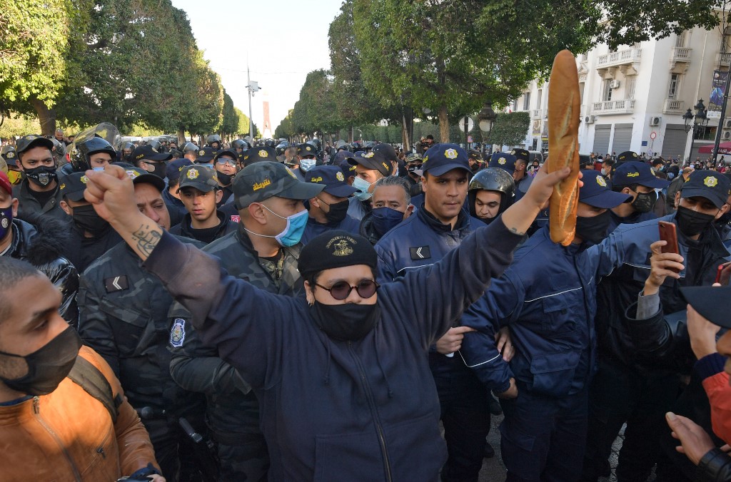 Un manifestant tunisien soulève une miche de pain alors que des agents de sécurité affrontent des manifestants lors d'un rassemblement antigouvernemental sur l'avenue Habib Bourguiba dans la capitale Tunis, le 19 janvier 2021. (Photo, AFP)