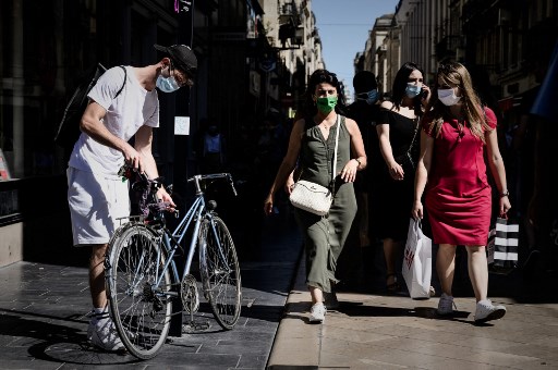 Un homme portant un masque de protection déverrouille son vélo alors que des femmes passent avec des sacs à provisions dans une rue, à Bordeaux, le 18 juillet 2020. (Philippe Lopez/AFP)