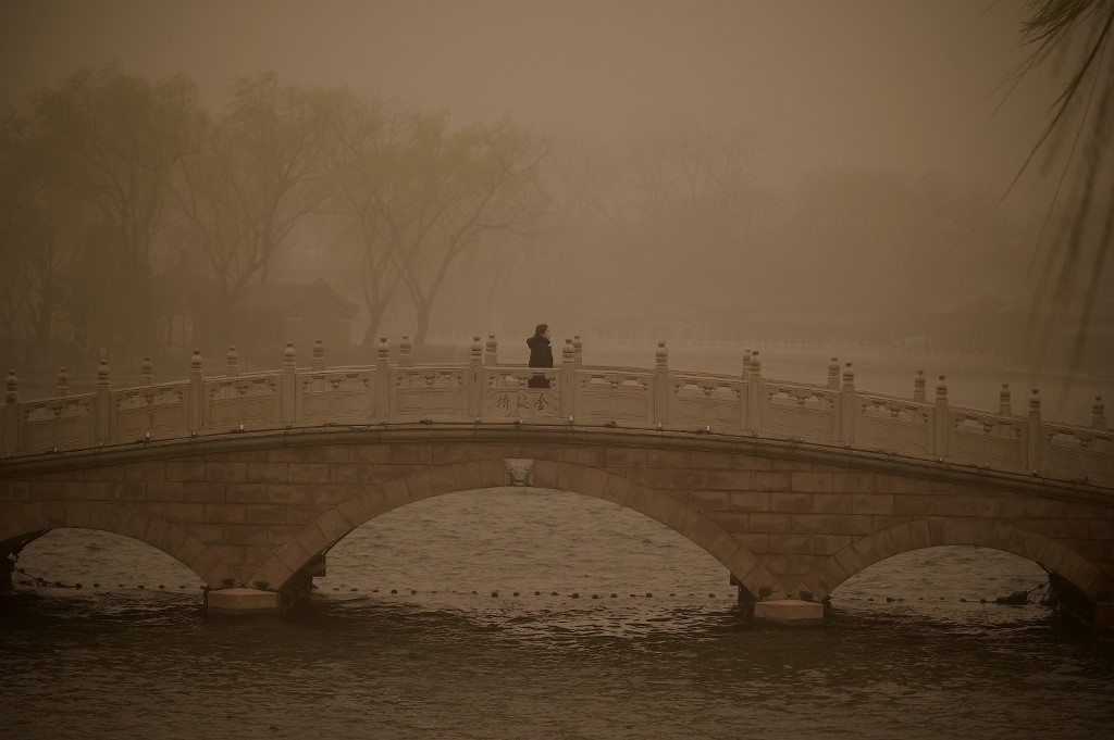 Une femme traverse un pont au lac Houhai lors d'une tempête de sable à Pékin le 15 mars 2021. Noel Celis / AFP