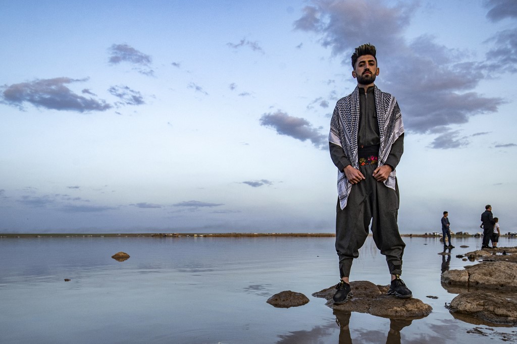 Un homme se tient debout sur un rocher, devant le réservoir d'eau de Mazqaft près de Qahtaniyah, dans le nord-est de la province syrienne de Hasakah, pendant les célébrations du Nouvel An kurde syrien persan, le Noruz, le 21 mars 2021 (AFP)