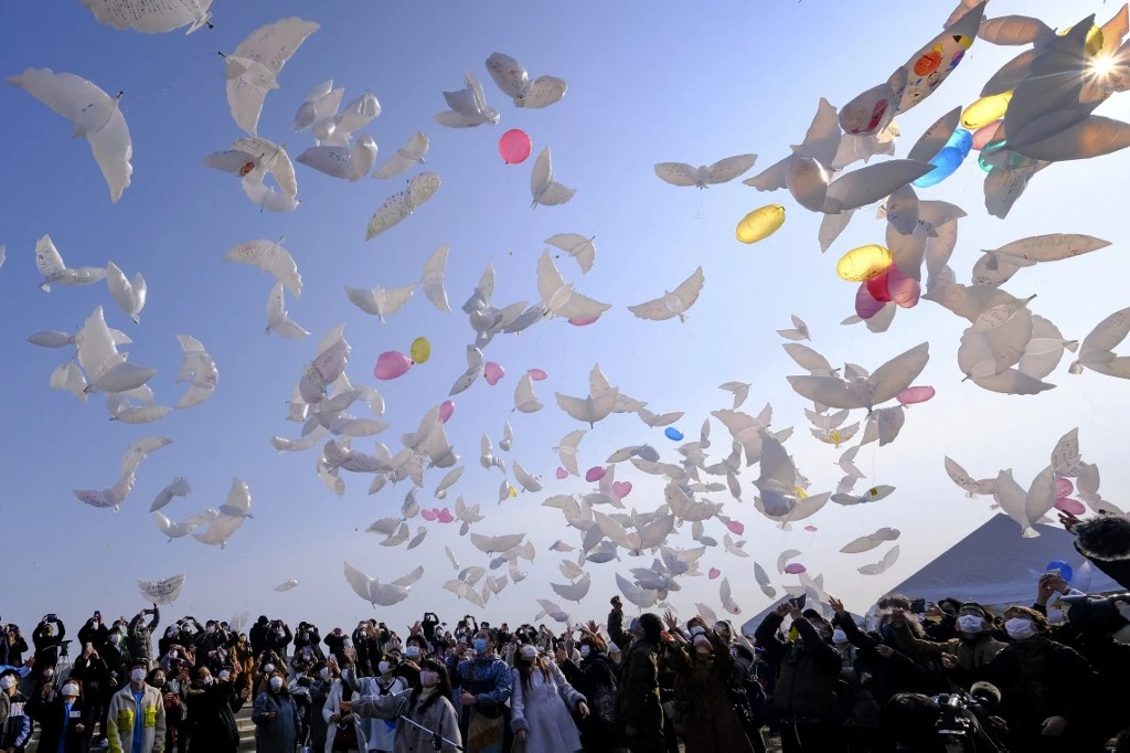 Des gens lâchent des ballons en forme de colombe dans le ciel pour pleurer les victimes du tremblement de terre et du tsunami à Natori, dans la préfecture de Miyagi, le 11 mars 2021, le 10e anniversaire du séisme de magnitude 9,0 qui a déclenché un tsunami et une catastrophe nucléaire qui a tué plus de 18000 personnes. Kazuhiro NOGI / AFP